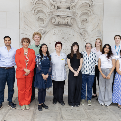 13 staff members, some wearing uniform and some wearing their own clothes, stood in front of the sign for the Royal Ear Hospital the
