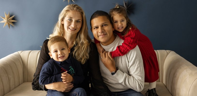 Jacob sitting on sofa with his mum, dad and sister, in front of a navy blue wall