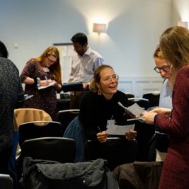 A busy room with people chatting and leaning towards each other.