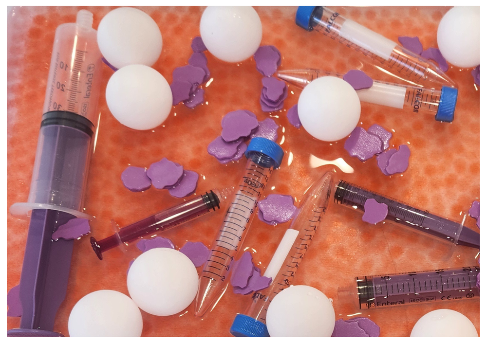 Assorted laboratory items including syringes, plastic sample tubes, white spheres and small purple shapes arranged on an orange textured surface