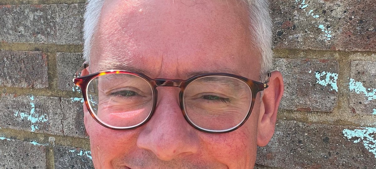 A man in glasses smiles broadly at the camera in bright sunshine