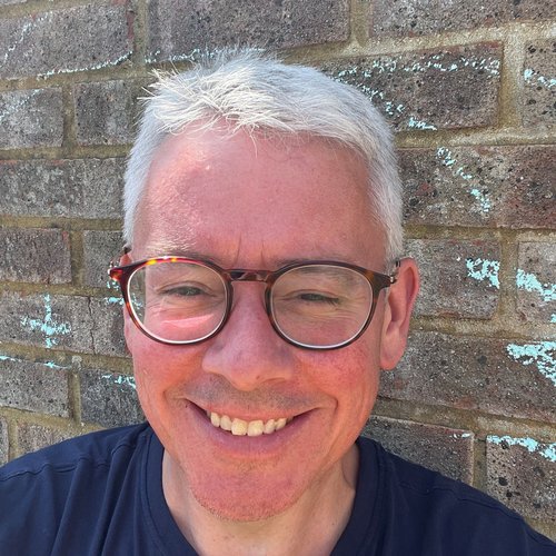 A man in glasses smiles broadly at the camera in bright sunshine