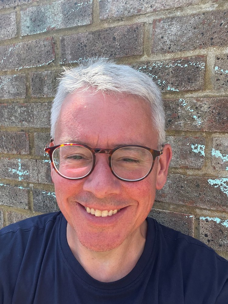 A man in glasses smiles broadly at the camera in bright sunshine