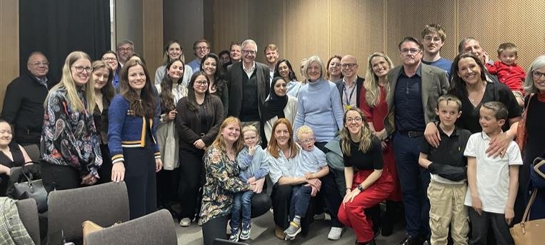 A group of colleagues, patients and family of Professor Chris Lloyd standing together in a room smiling.