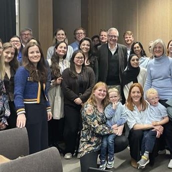 A group of colleagues, patients and family of Professor Chris Lloyd standing together in a room smiling.