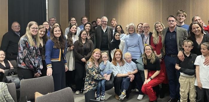 A group of colleagues, patients and family of Professor Chris Lloyd standing together in a room smiling.