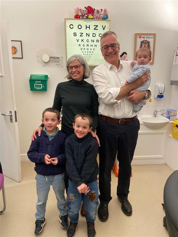 A doctor and his partner pictured with two patients and a baby in a clinic room