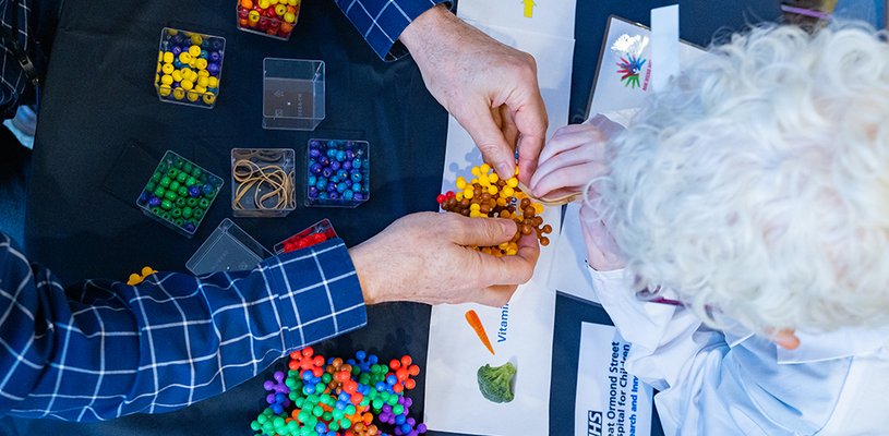 A view from above of adult hands playing with some scientific models and the top of a child's head. The child has bright white hair and is wearing a lab coat. You can't see their faces
