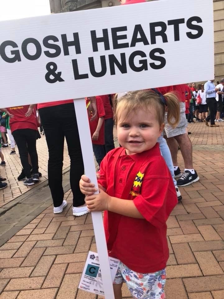 Patient holding sign that says GOSH heart and lungs. They are smiling at the camera.