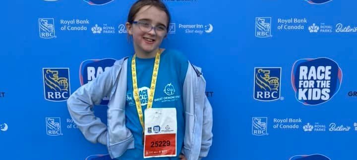 Sophia standing in front of a blue banner with Race for the Kids and GOSH Charity logos