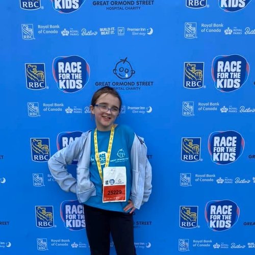 Sophia standing in front of a blue banner with Race for the Kids and GOSH Charity logos