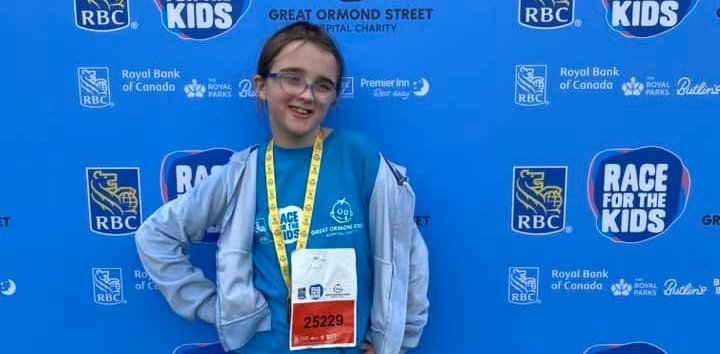 Sophia standing in front of a blue banner with Race for the Kids and GOSH Charity logos