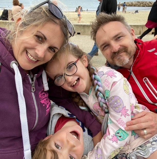 Sophia with her mum to her left and her dad to her right, and her younger brother below sat in front of a beach