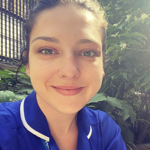 A woman in a blue nurse's uniform smiles at the camera