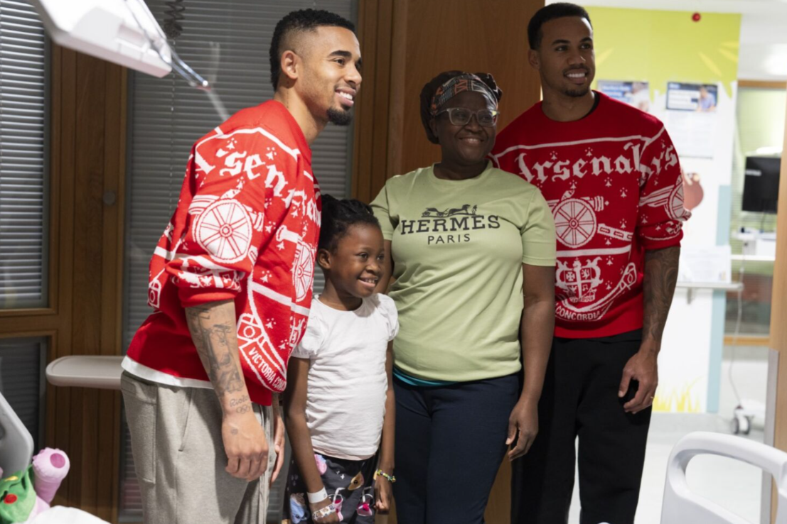 2 arsenal mens players taking photo on a ward with young girl and mum