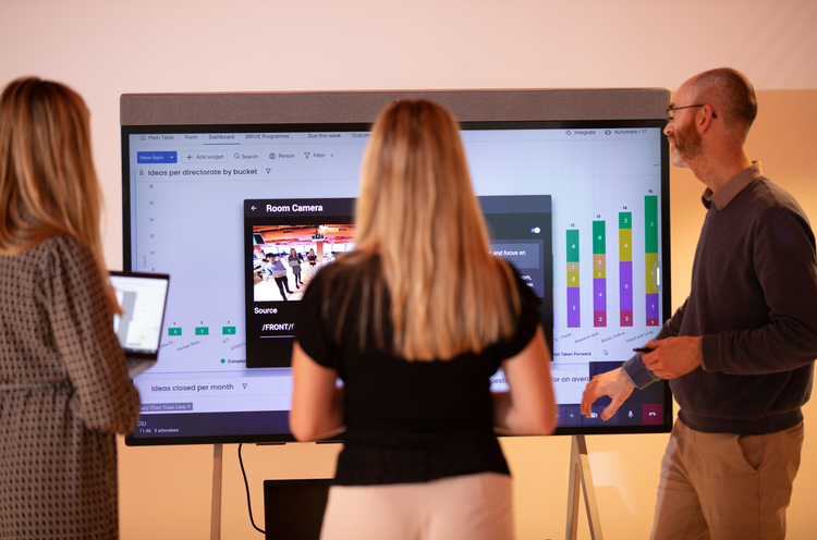 3 people stood looking at a large digital screen with some coloured bar charts