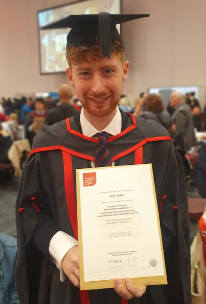 Boy wearing black graduation gown, smiling and holding degree papers