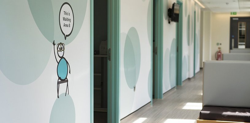 An inside shot of the Sight and Sound Centre, showing a corridor with clinical rooms. There is a cartoon figure on the wall and a speech bubble reads "This is waiting area B"