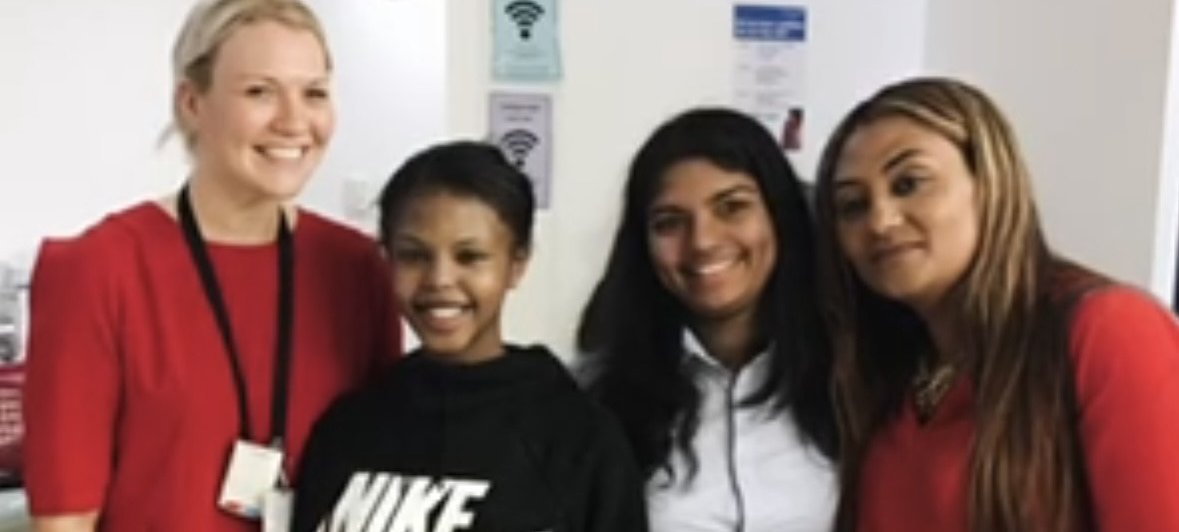 Woman with blonde hair dressed in red, stood next to two girls with brown hair in black, next to a woman with light brown and blonde hair in black