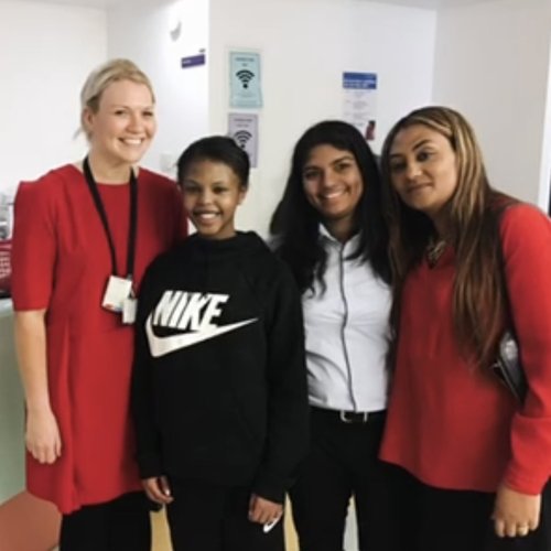 Woman with blonde hair dressed in red, stood next to two girls with brown hair in black, next to a woman with light brown and blonde hair in black