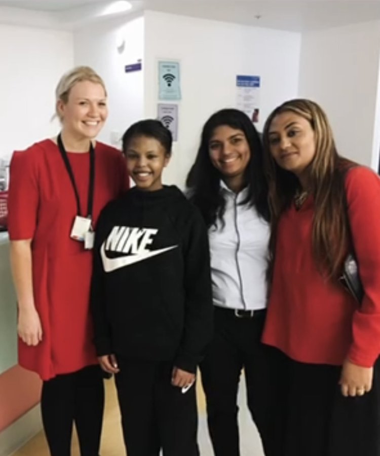 Woman with blonde hair dressed in red, stood next to two girls with brown hair in black, next to a woman with light brown and blonde hair in black