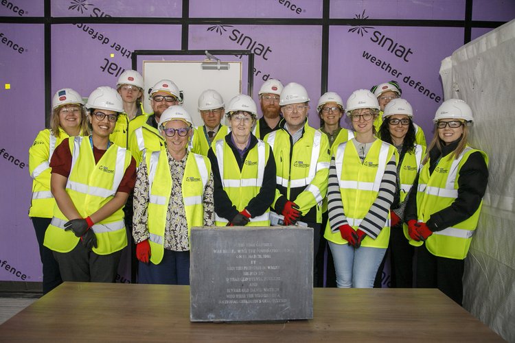 A group of staff wearing high visibility vests, hard hats, gloves and goggles with a time capsule