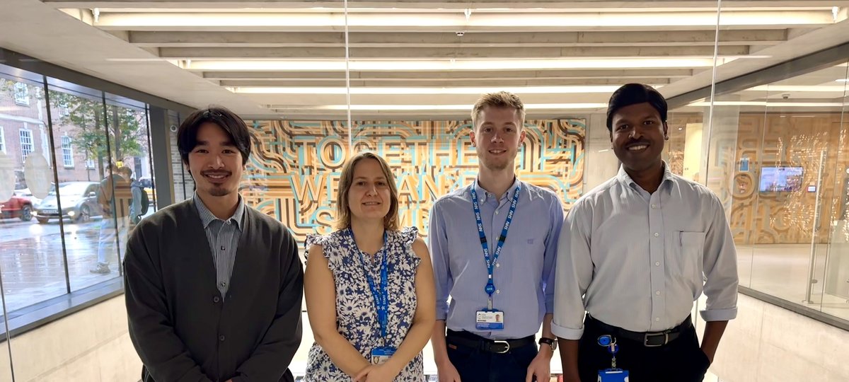 Four members of staff standing in ZCR atrium in front of windows that look over labs