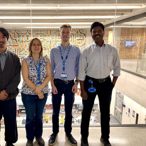 Four members of staff standing in ZCR atrium in front of windows that look over labs