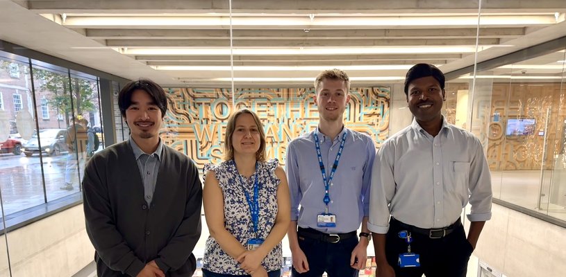 Four members of staff standing in ZCR atrium in front of windows that look over labs