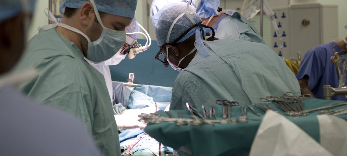 A surgical theatre showing the backs of surgeons operating and lots of bright lights