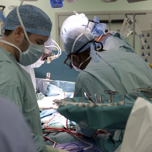 A surgical theatre showing the backs of surgeons operating and lots of bright lights