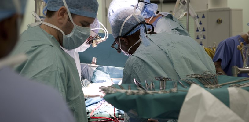 A surgical theatre showing the backs of surgeons operating and lots of bright lights