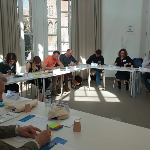 Group of adults sat around a large U-shaped table and writing on post-it notes.