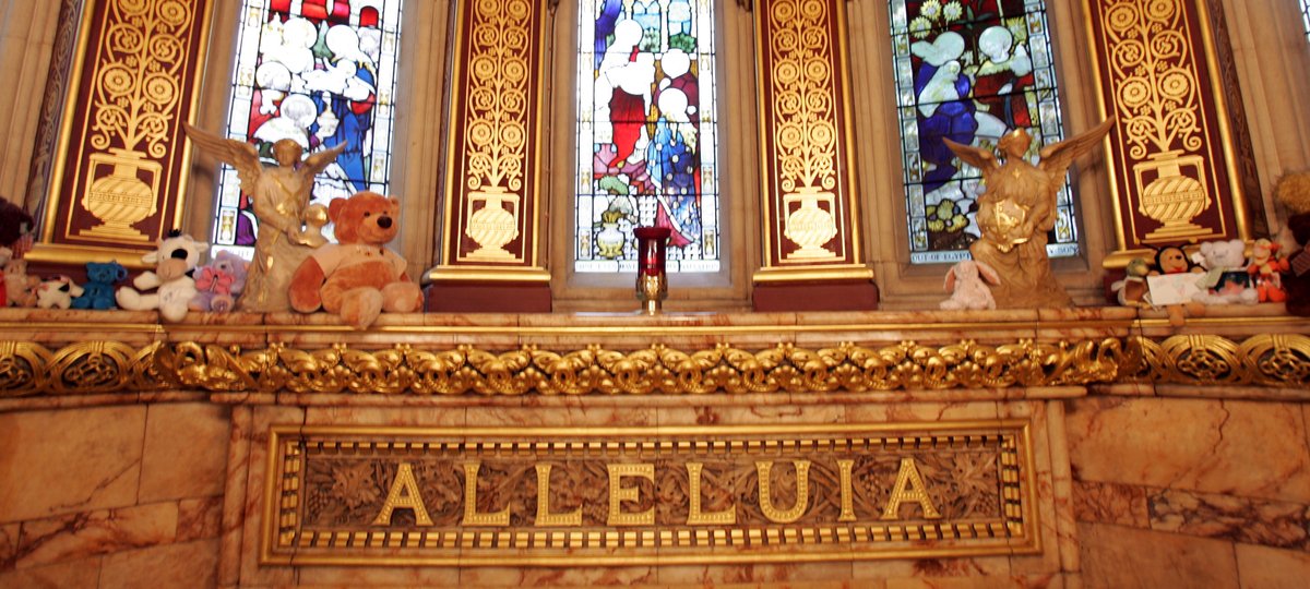 Photo of the altar inside St. Christopher's Chapel at GOSH. The word "Allelluia" is visible and small teddy bears and photos of children have been placed at the altar.