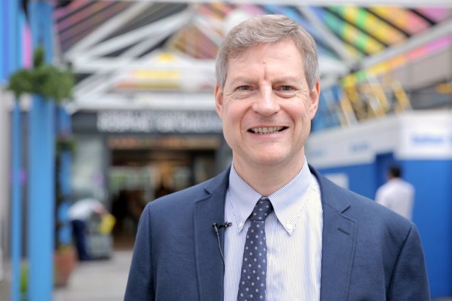 Professor Thomas Voit stands in front of the GOSH entrance in a blue suit and spotty tie