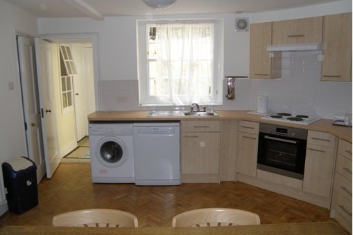 Staff accommodation kitchen featuring washing machine, small refrigerator, sink, oven, and hob.