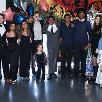A group of young people in smart suits and party outfits. Colourful balloons behind.