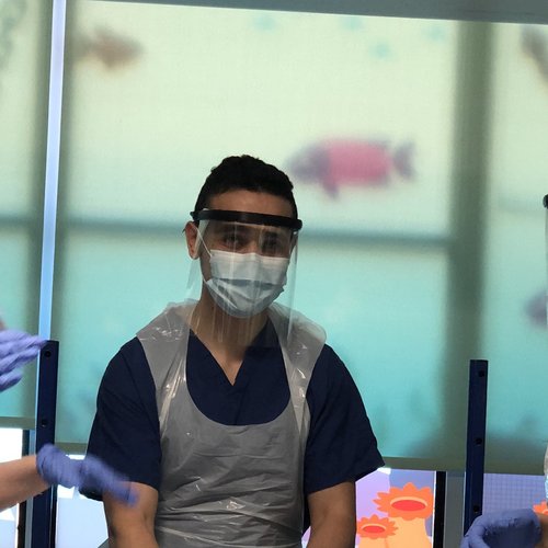 Photo of four female doctors and nurses wearing blue scrubs, white aprons, face masks and face shields